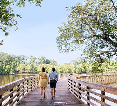 A couple walks hand in hand on a bridge over a lake