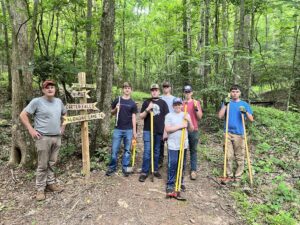 A group of people pose with trail tools while working on a trail.